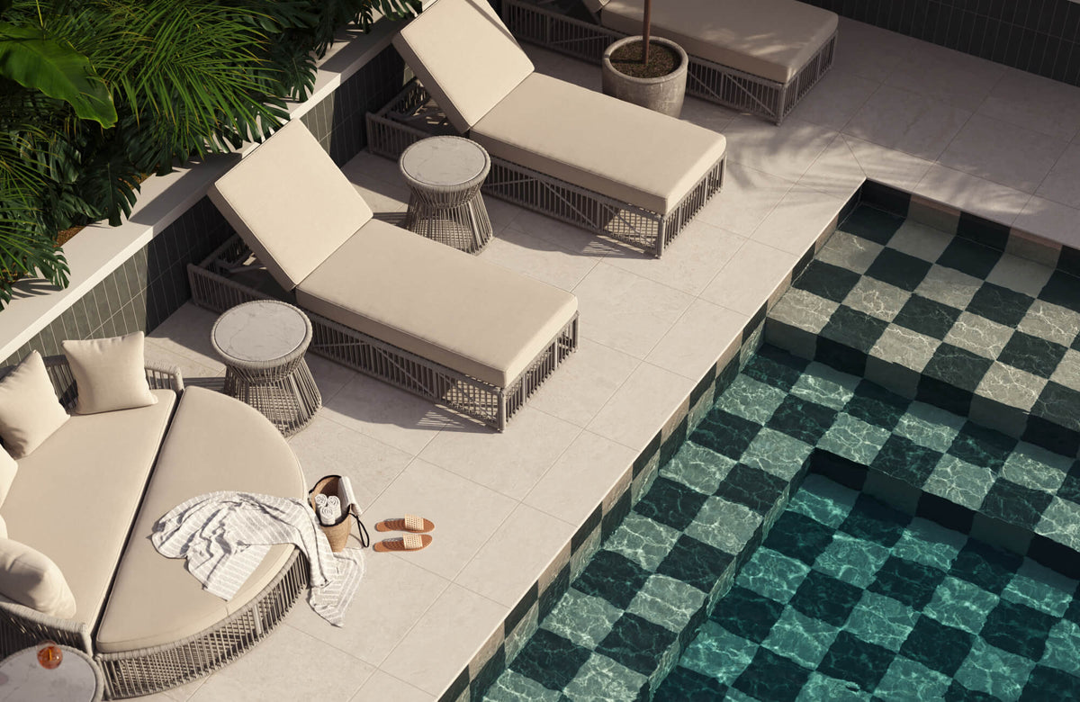 Sun-drenched patio with tan rope loungers, white cushions, and a circular sofa beside a shiny green tiled pool and tropical palms.