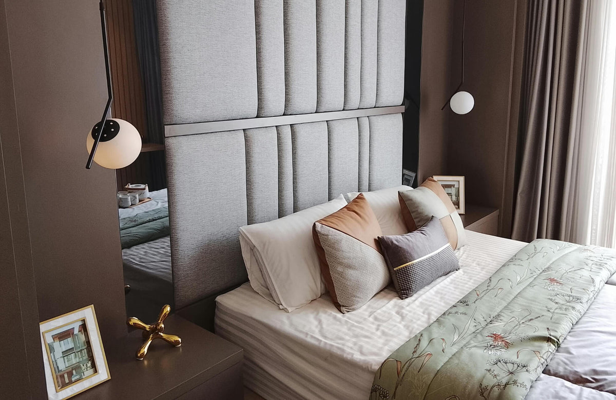 Modern bedroom with layered decorative pillows in neutral and warm tones against a tall upholstered headboard and soft ambient lighting.