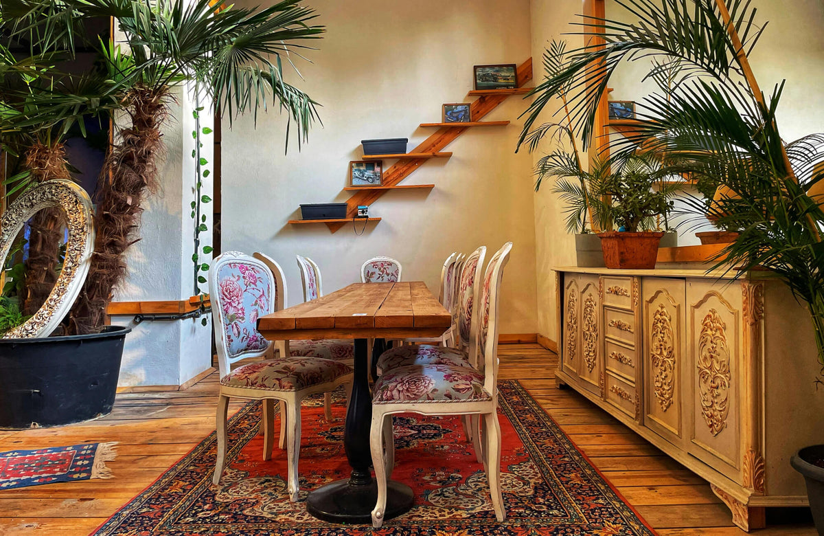 Red Persian rug anchors a cozy sitting area with mixed seating, warm wood tones, greenery, and layered textures.
