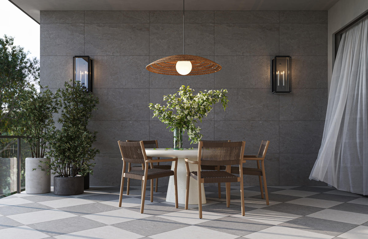 Outdoor dining area with checkered tile floor, gray stone look wall tiles, dining table with wood chairs, sconces, and a woven pendant light.