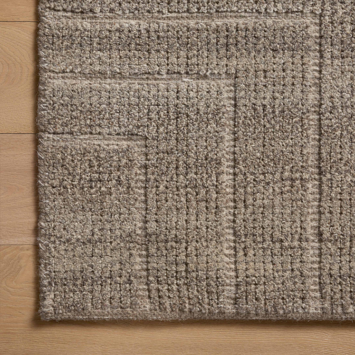 A close-up view of a brown rug with a dense, hand-loomed texture, showing subtle tonal shifts and angular lines that create a softly geometric pattern.