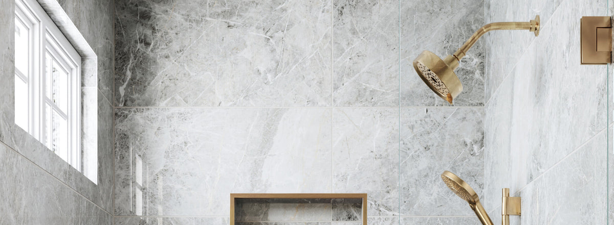 Luxurious shower with grey marble look tiles and dual brass showerheads, complemented by a built-in shelf and a window for natural light