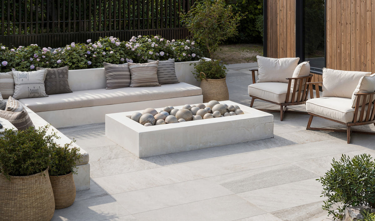 Elegant outdoor patio with stone-look tiles, featuring comfortable seating, a modern fire pit, and lush greenery