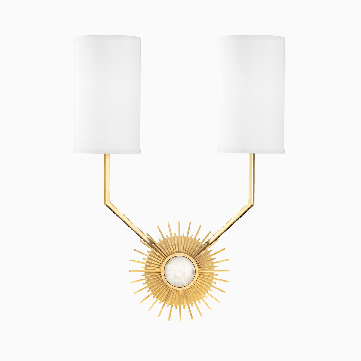 Aged brass wall sconce with dual white cylindrical shades and radiant sunburst backplate, blending bold geometry with modern elegance.