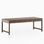 A rectangular walnut dining table with a matte brown finish, shown with a flat, expansive top and minimalist base where slender legs are joined at the ends.