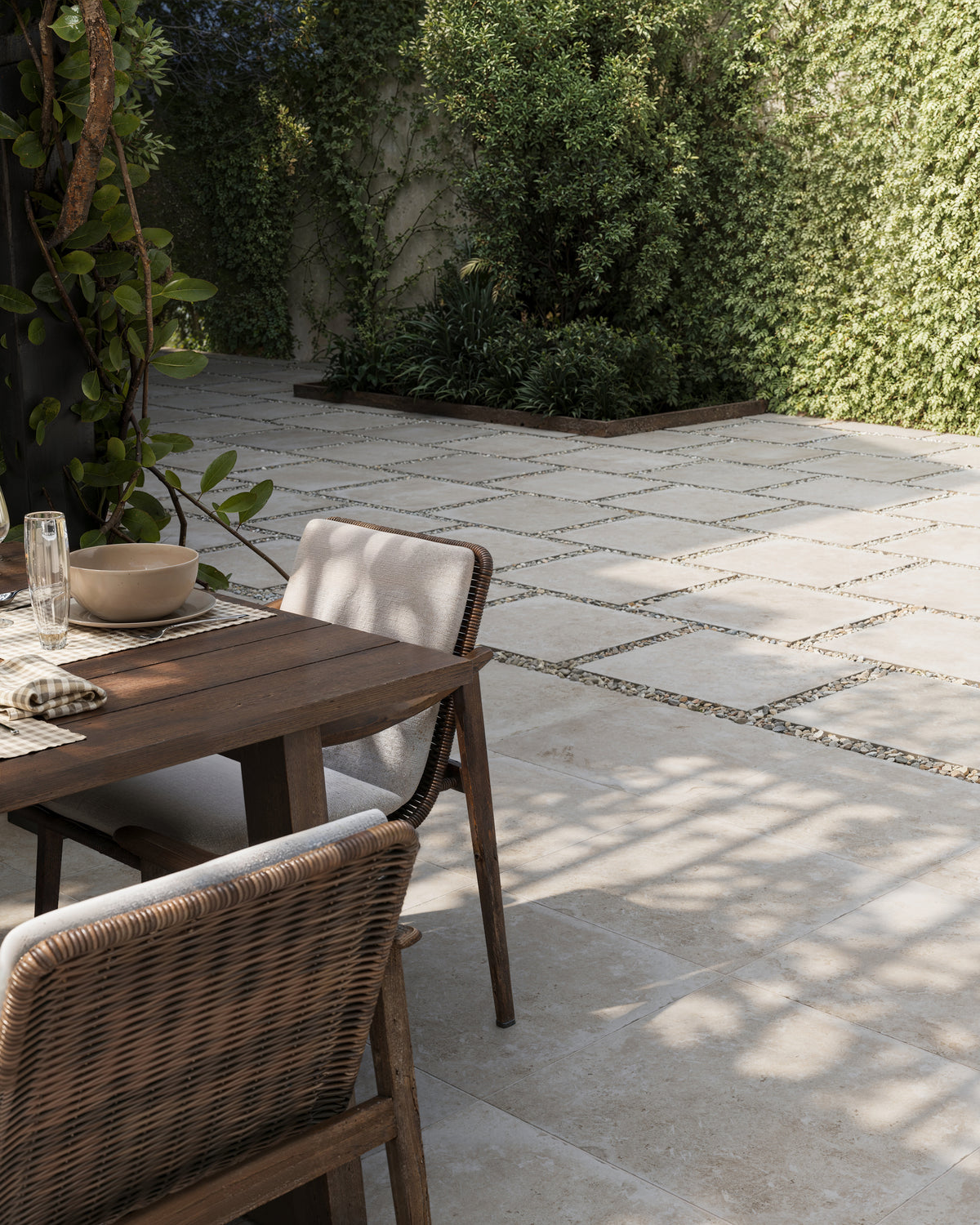 Charming patio scene showcasing Bowden 24x24 Grip Porcelain Pavers in Oat, surrounded by lush greenery for a serene atmosphere.