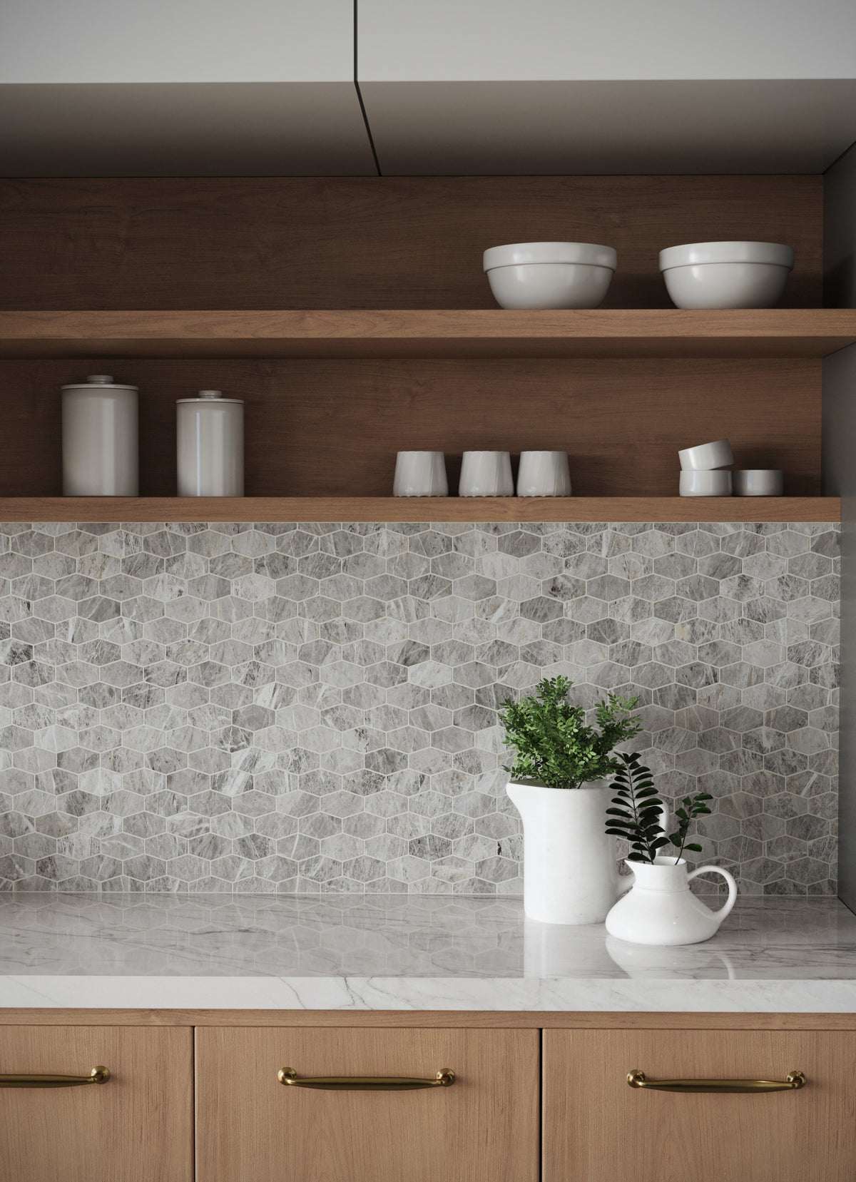 Close-up of a kitchen backsplash featuring polished hexagonal mosaic tiles in grey, warm wooden open shelving, brass-accented cabinetry, and decorative greenery on a marble-look countertop. 