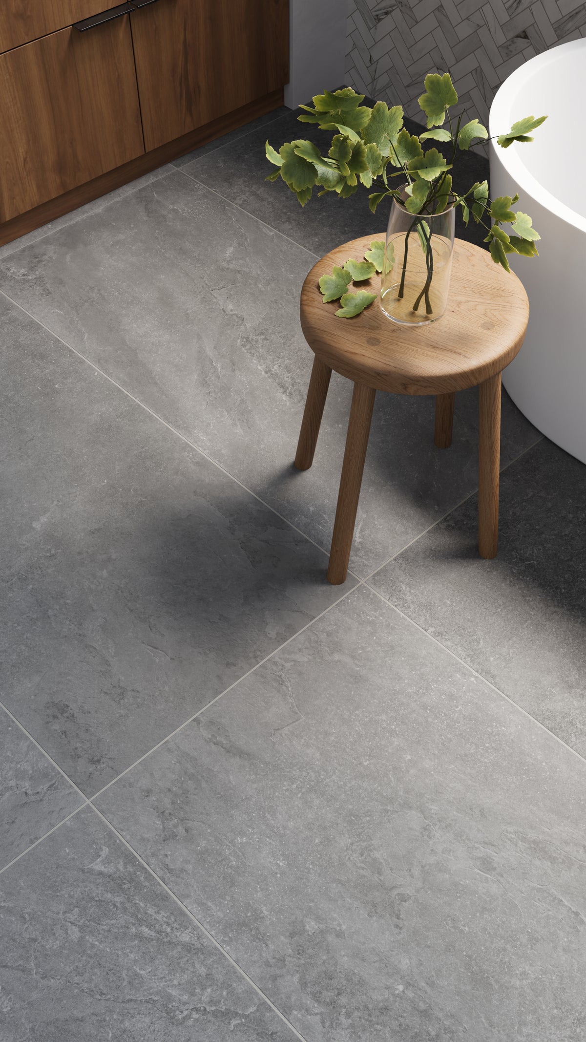 Elegant charcoal-toned floor tiles with subtle veining bring a natural stone aesthetic to this modern bathroom, complemented by a wooden stool and fresh greenery.