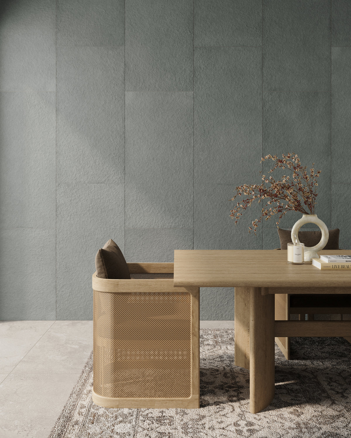 A dining area with a wooden table and a rattan chair, set against a green-gray Palmer raw porcelain tiled wall for a natural look.
