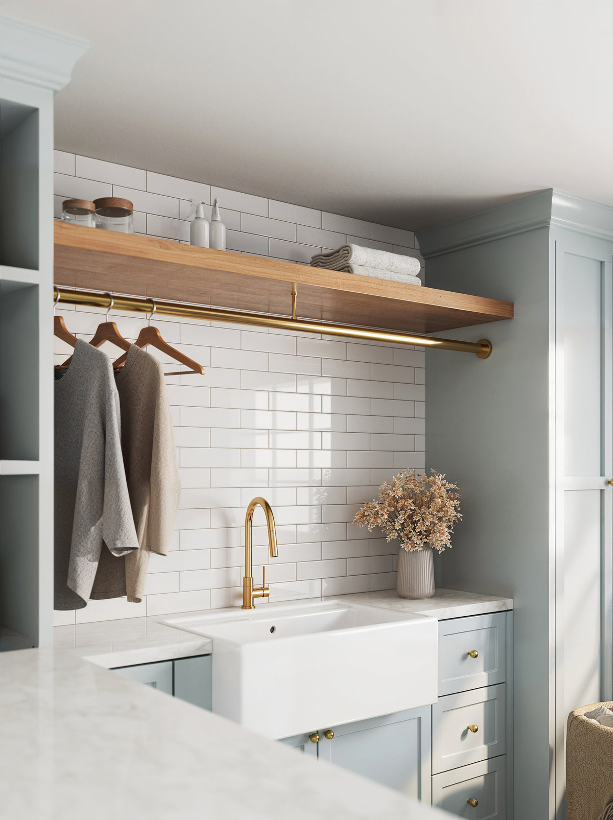 Elegant laundry space featuring Polly White 3x10 glossy ceramic tiles, a farmhouse sink, light blue cabinets, and brass accents for a timeless, polished look.