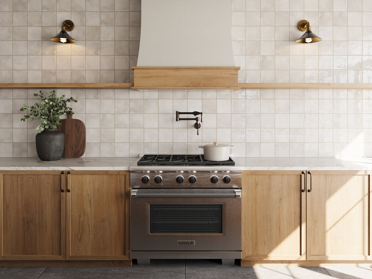 Bright kitchen featuring Lilah Mist 6x6 glossy tiles as a backsplash, a stainless steel range, wooden cabinets, and brass wall sconces.