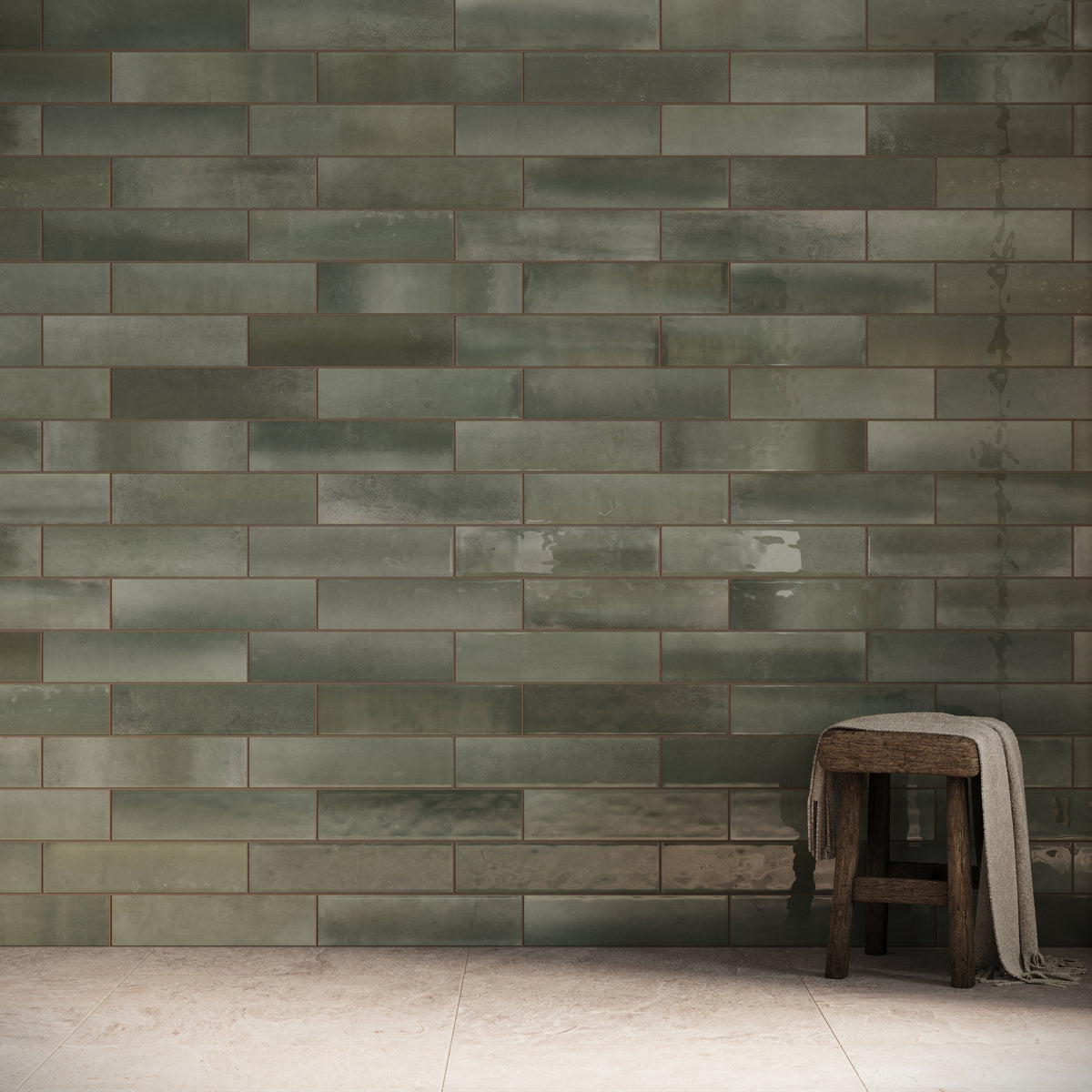 Glossy green subway tiles create a serene feature wall, paired with neutral stone flooring and a rustic wooden stool draped with a soft towel.