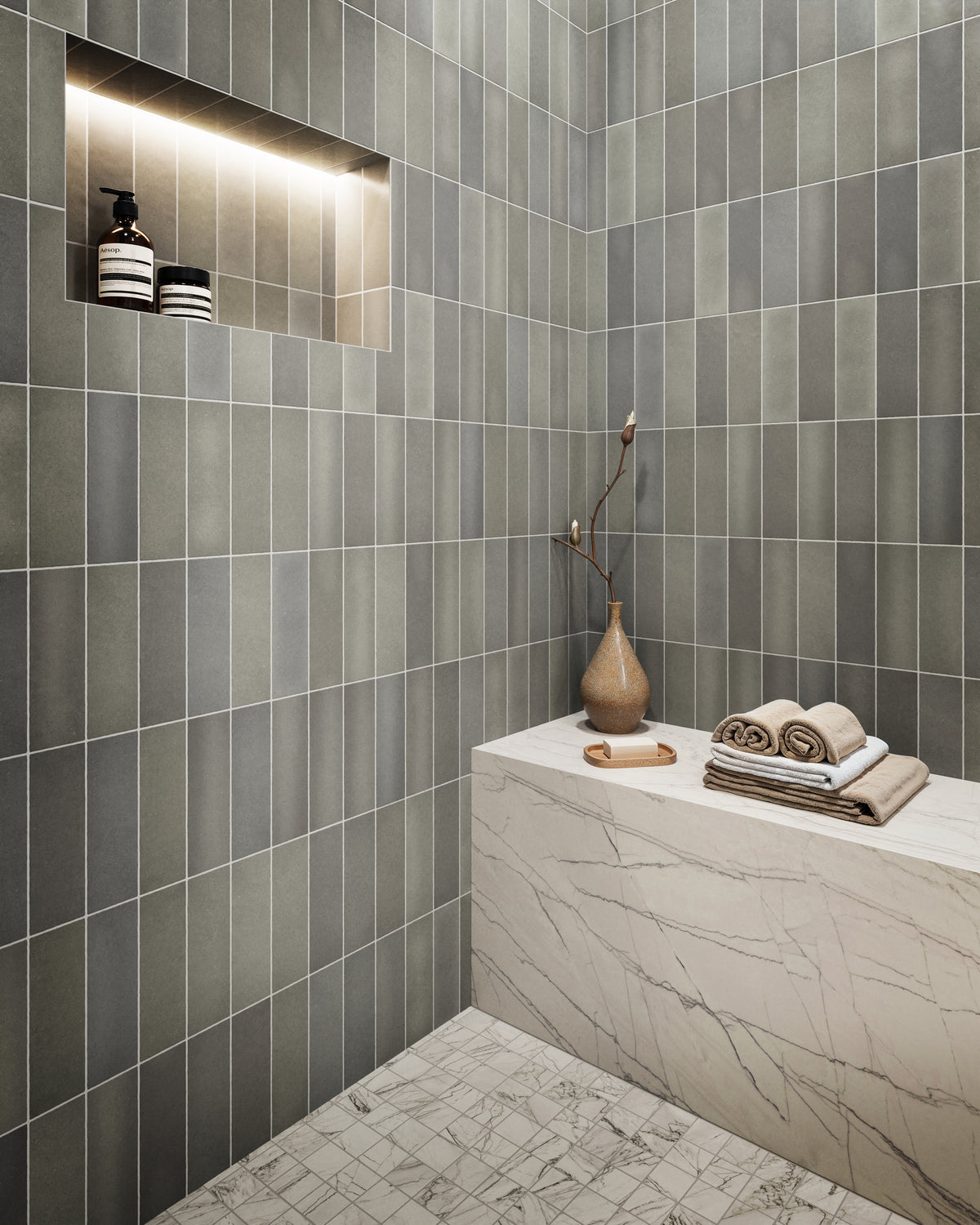 A tranquil bathroom showcasing matte pebble-toned tiles, a marble bench with elegant veining, and mosaic marble floors, creating a serene and sophisticated retreat.
