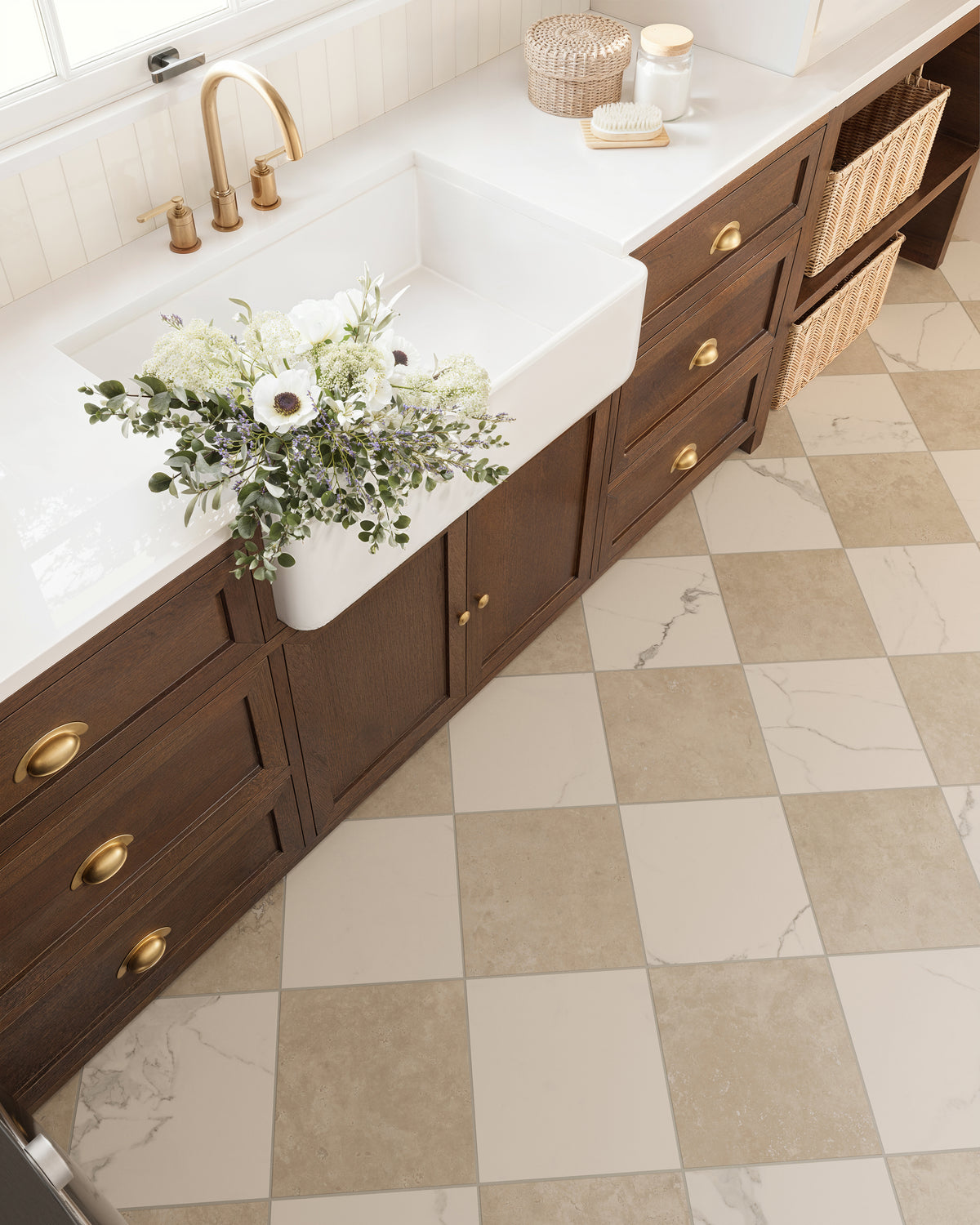 Overhead view of a laundry sink with a bouquet of white flowers, white subway tile backsplash installed vertically, dark wood cabinetry with gold hardware, and a checkerboard tile floor