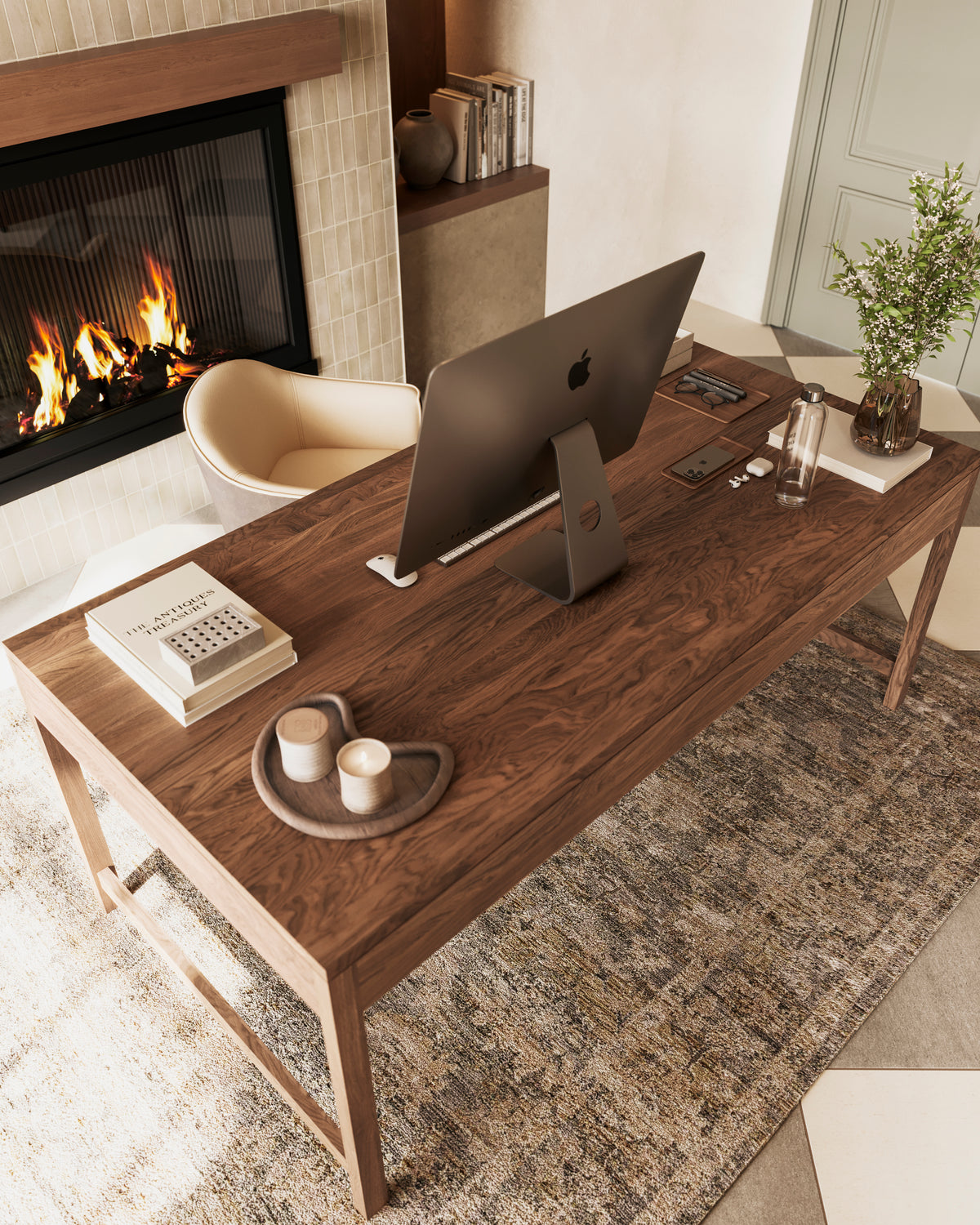 A rectangular walnut desk with visible wood grain and slender legs, styled with books and a desktop setup beside a fireplace, ideal for relaxed, refined workspaces.