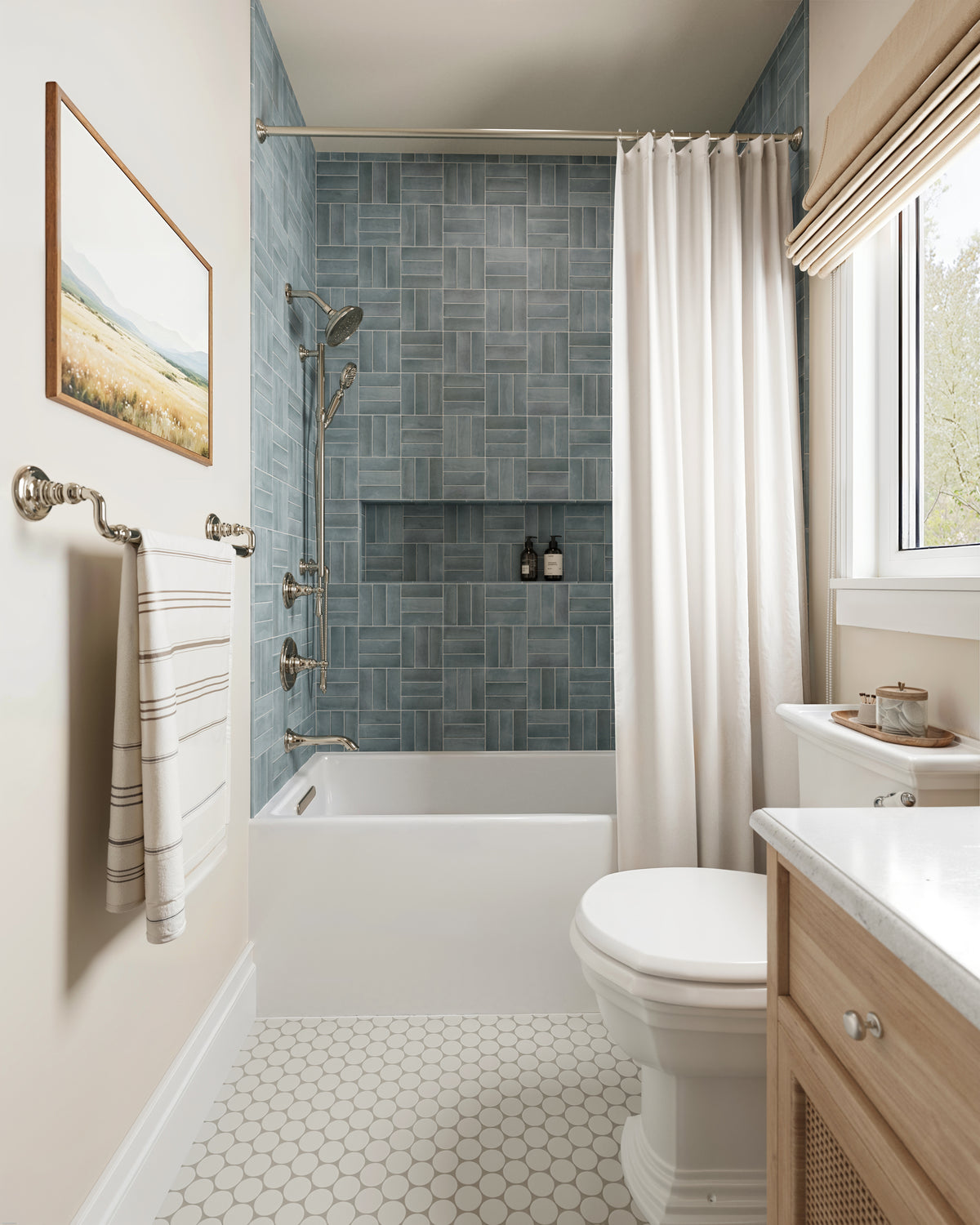 Natasha 0.5x8 matte ceramic tile trim in Ice, framing soft blue shower tiles above white hexagon floor tiles in a serene, sunlit bathroom.