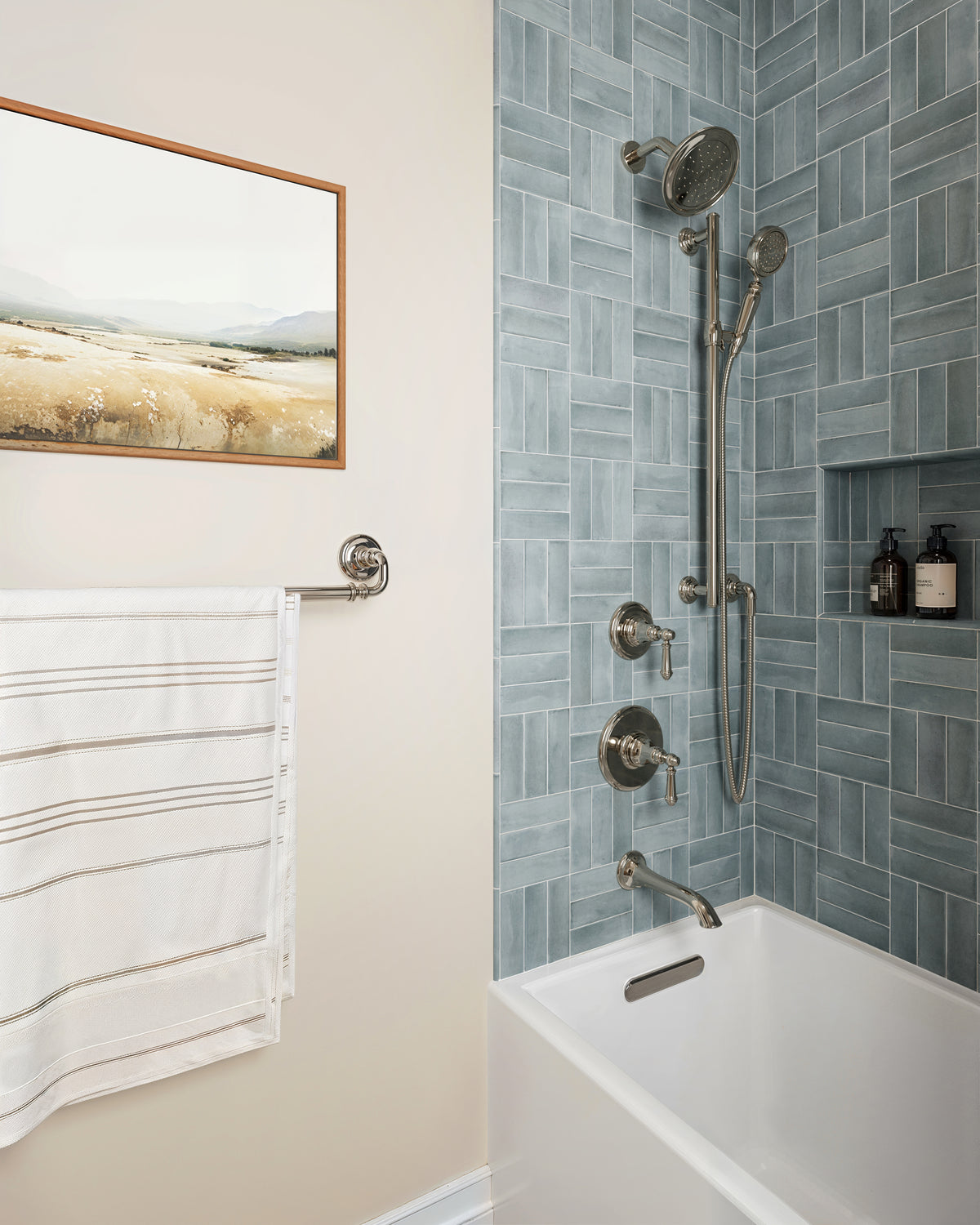 Natasha 0.5x8 matte ceramic tile trim in Ice outlines a cool-toned shower wall of blue porcelain tiles, paired with a clean white tub and polished chrome fixtures.