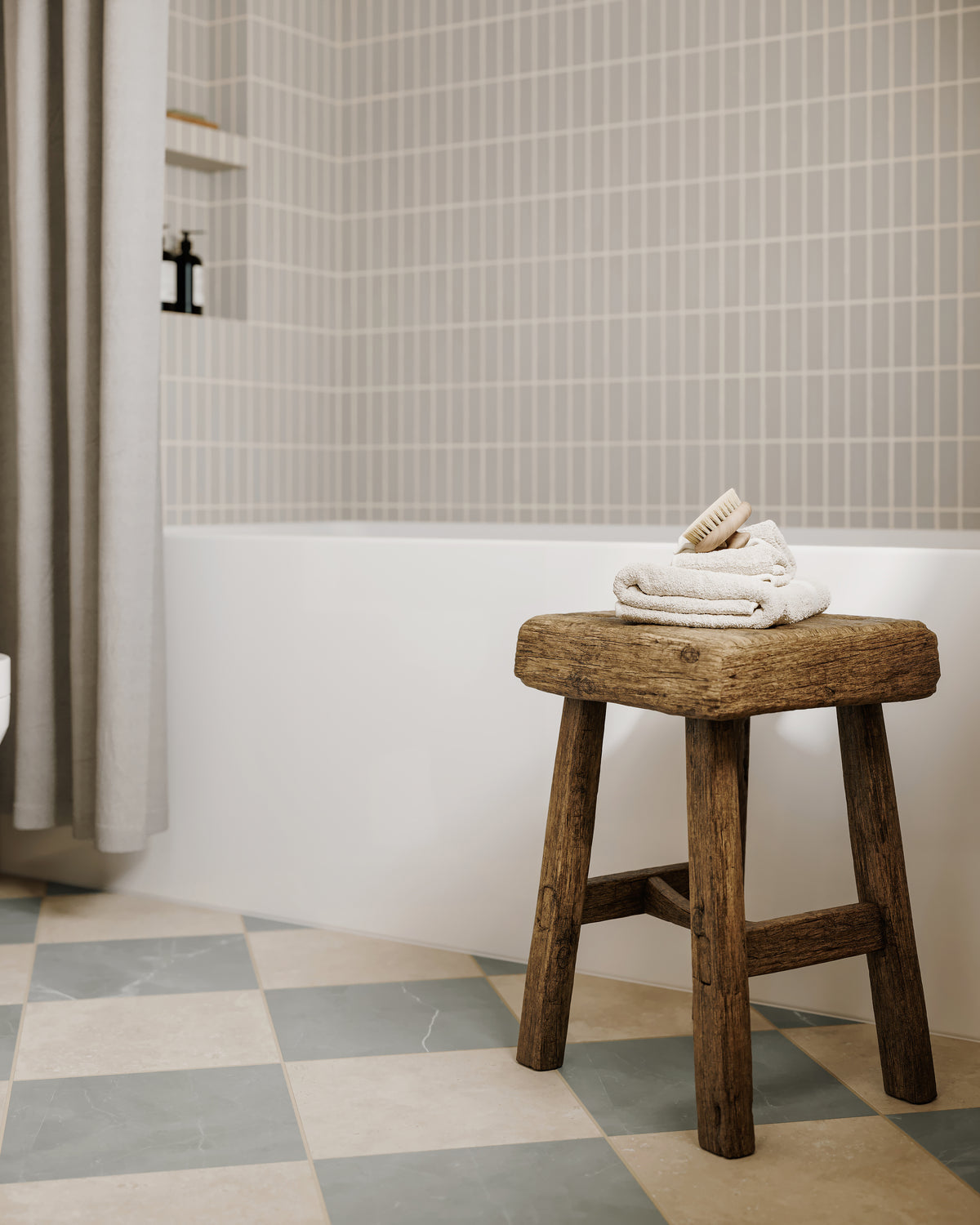Serene bathroom with checkerboard floor tiles, subway sage wall tile, and rustic wood stool topped with folded towels and a brush.