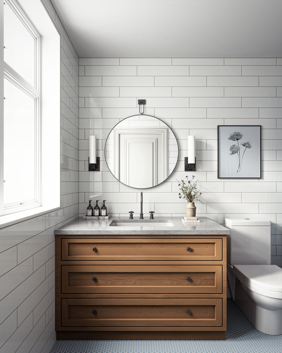 Vanity view of a bathroom with wood cabinetry, round mirror, white subway tile walls, and soft blue penny tile flooring.