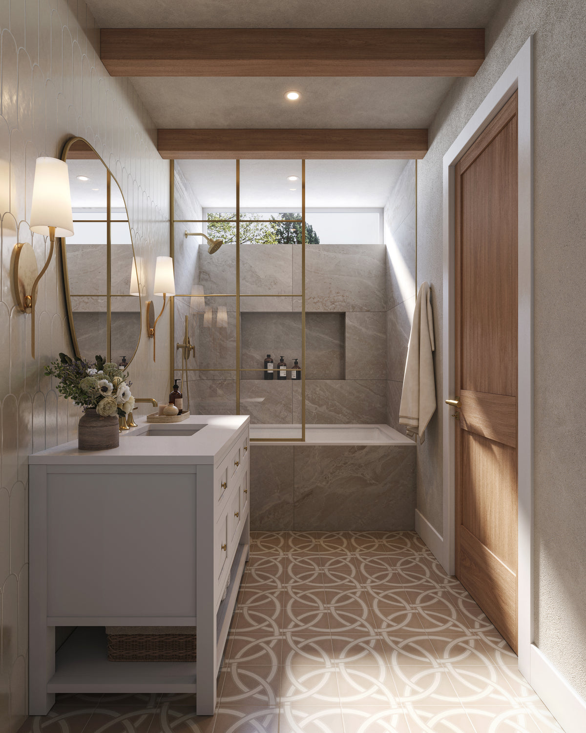 Narrow bathroom with a Bright White vanity and white quartz countertop beneath an organic-shaped mirror and brass sconces. The space features patterned floor tile, wood ceiling beams, a glass partition with brass framing, and a marble tub and shower area with a built-in niche.