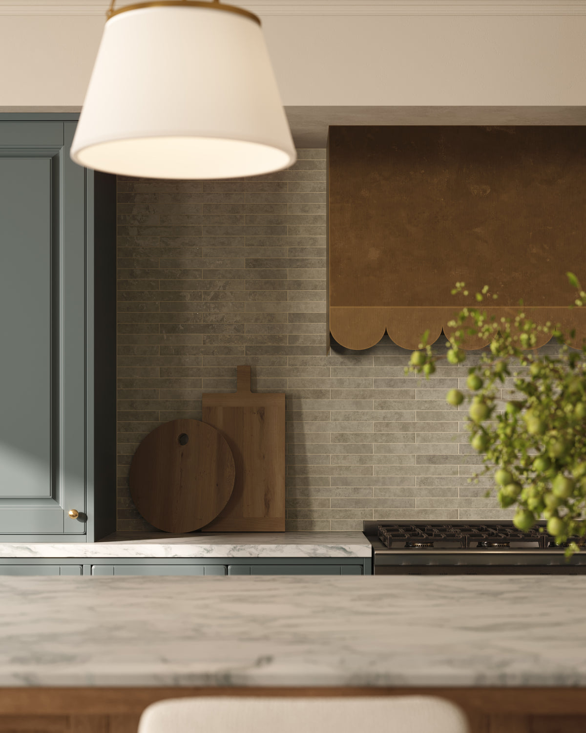 Close-up of a kitchen backsplash with muted green subway tile, a warm brass range hood, marble countertop, and soft pendant lighting for a refined, classic kitchen look.