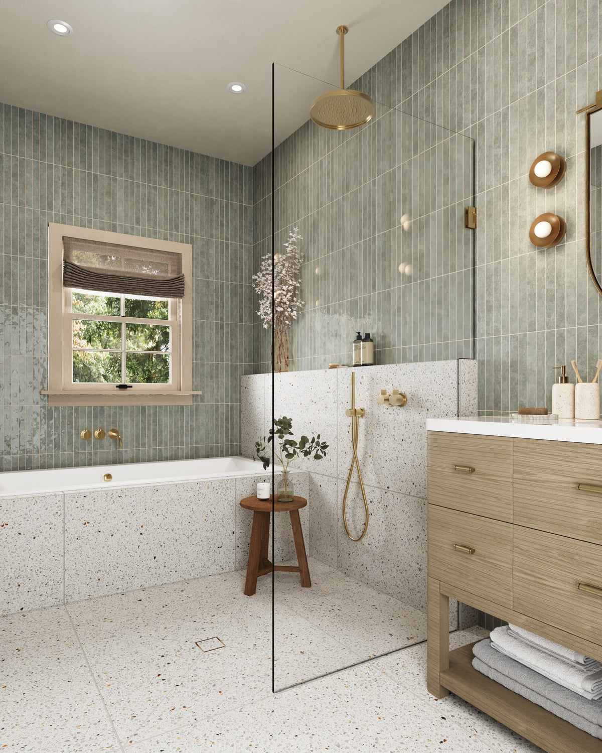 Bright spa-style bathroom featuring vertical green tile walls, terrazzo floors and shower surround, a glass partition, brass fixtures, and a wood vanity with integrated storage.