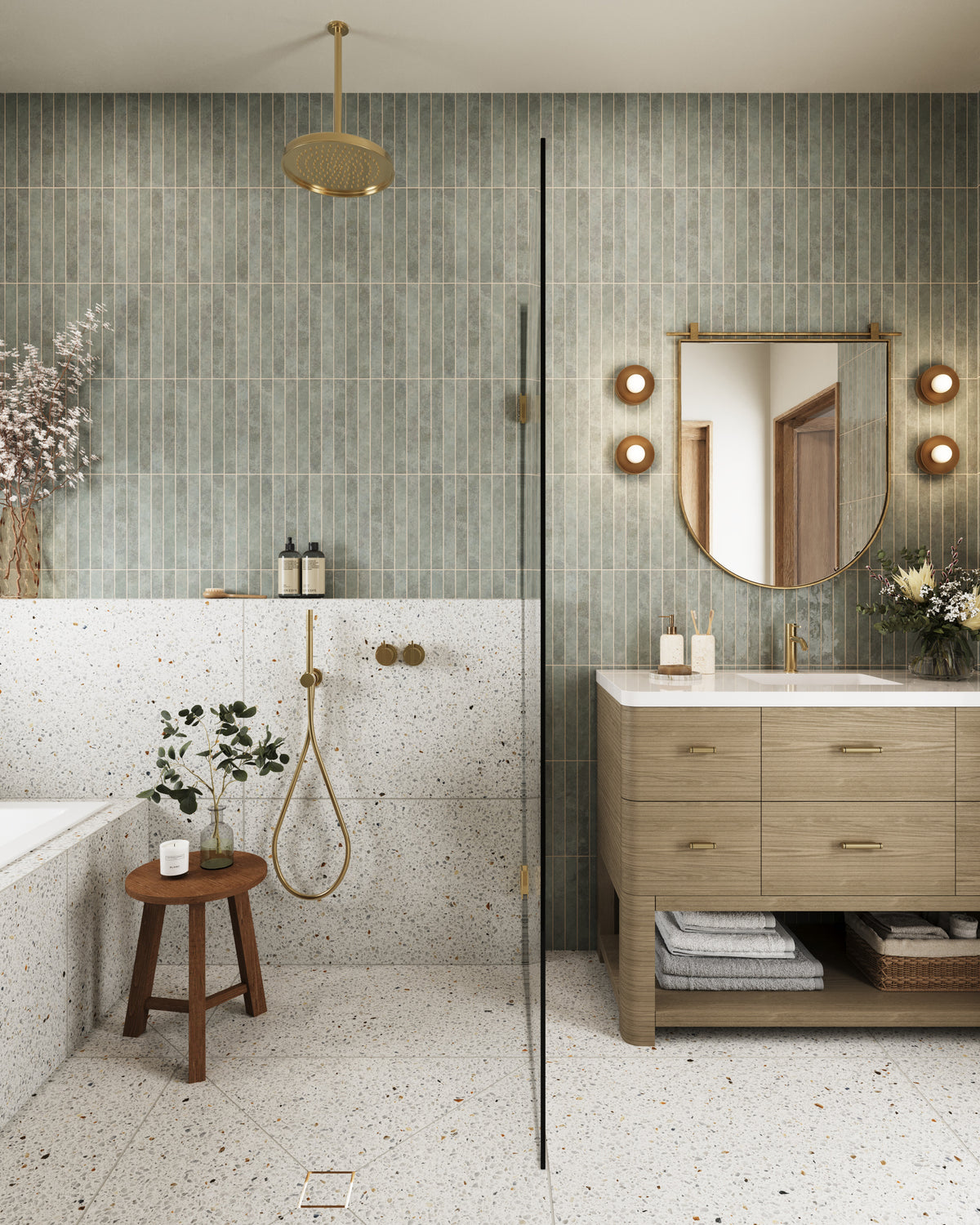Serene modern bathroom with vertical green tile walls, terrazzo shower surround, brass fixtures, a floating wood vanity, and soft layered lighting.
