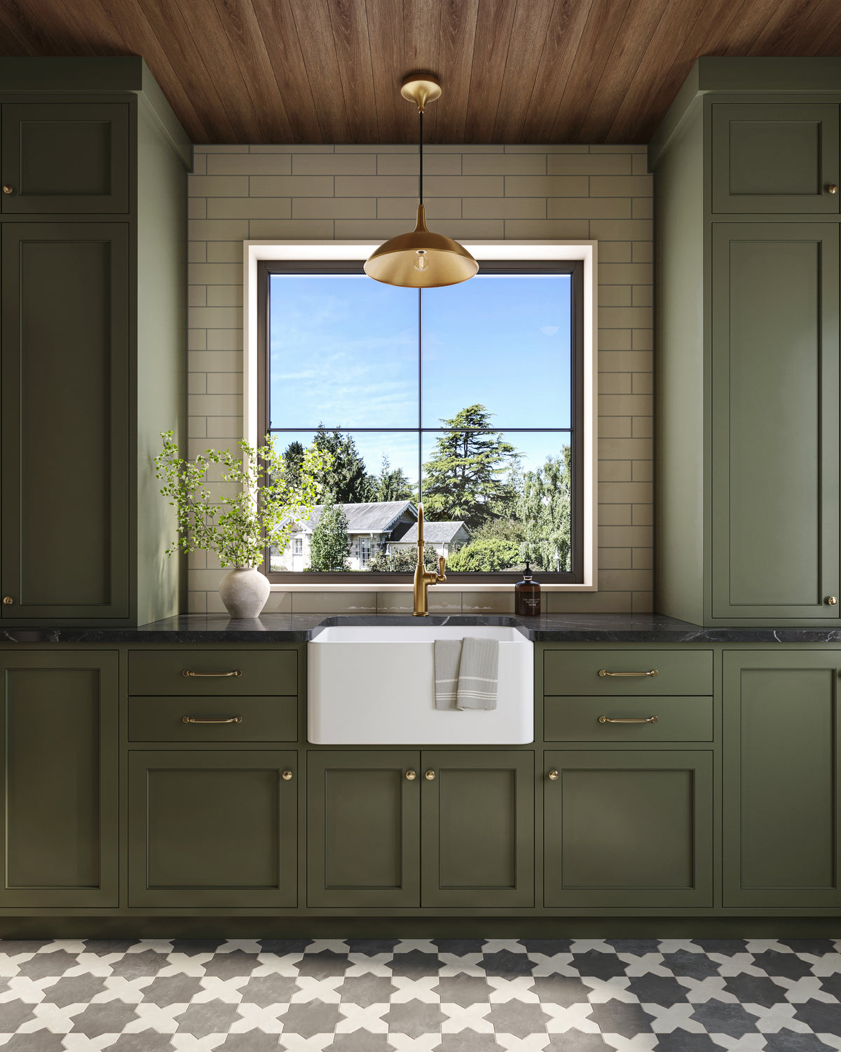 Green kitchen cabinets with farmhouse sink, brass faucet, patterned tile floor, and brushed gold pendant centered above the window