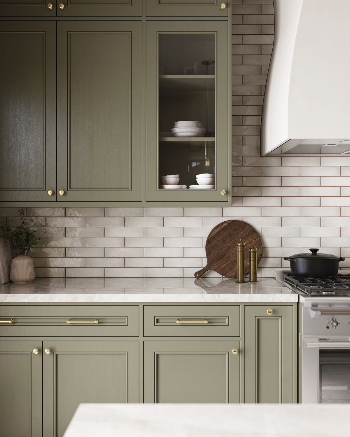 Glossy subway tiles in white-beige tones pair with sage green cabinetry, brass hardware, and marble countertops for a warm, elegant kitchen design.