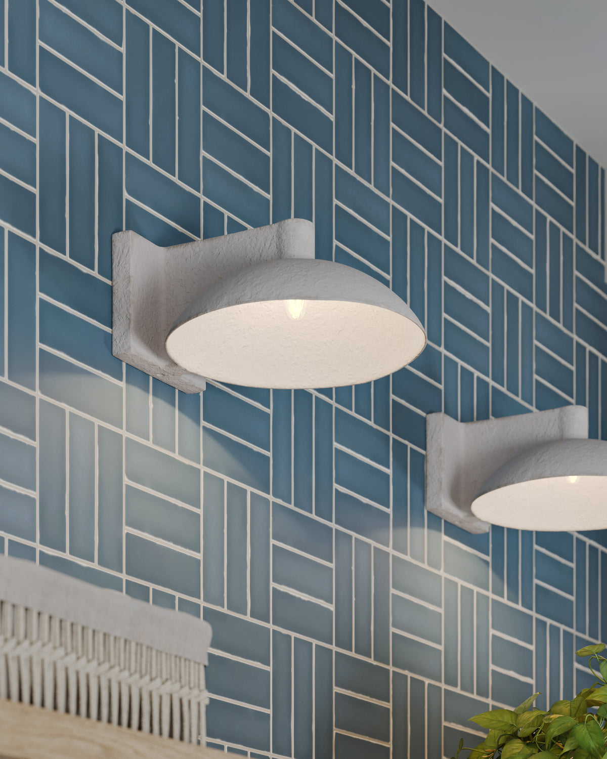 Pair of textured white dome wall sconces mounted on blue herringbone tile, casting soft ambient light in a modern interior