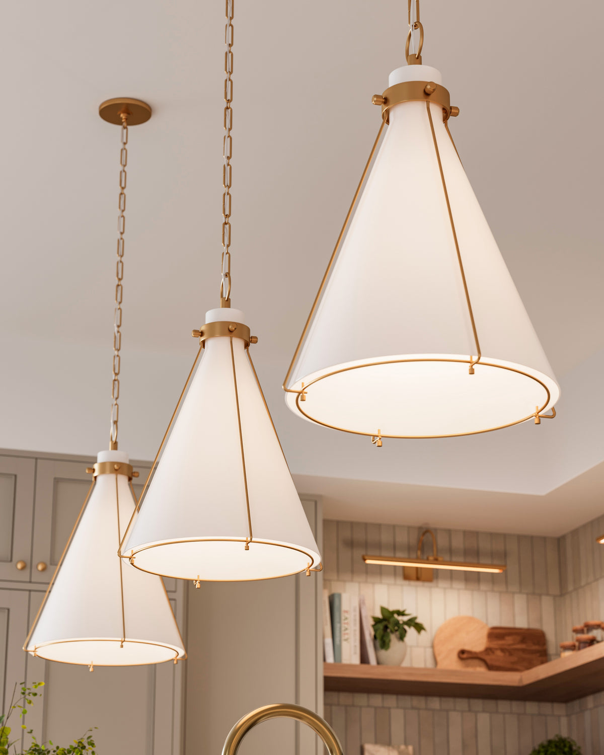 Three aged brass cone pendant lights with frosted glass shades hanging above a kitchen island, adding warm illumination and elegant symmetry.