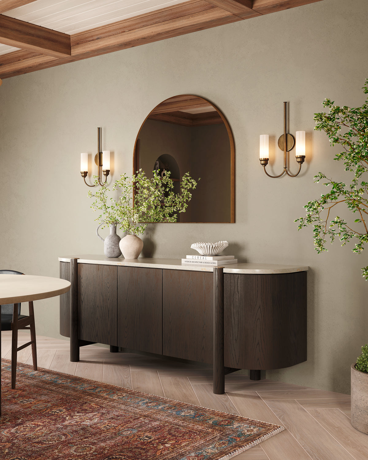 Dark wood sideboard styled with ceramic vases and greenery beneath an arched mirror and brass sconces in a warm, refined interior.