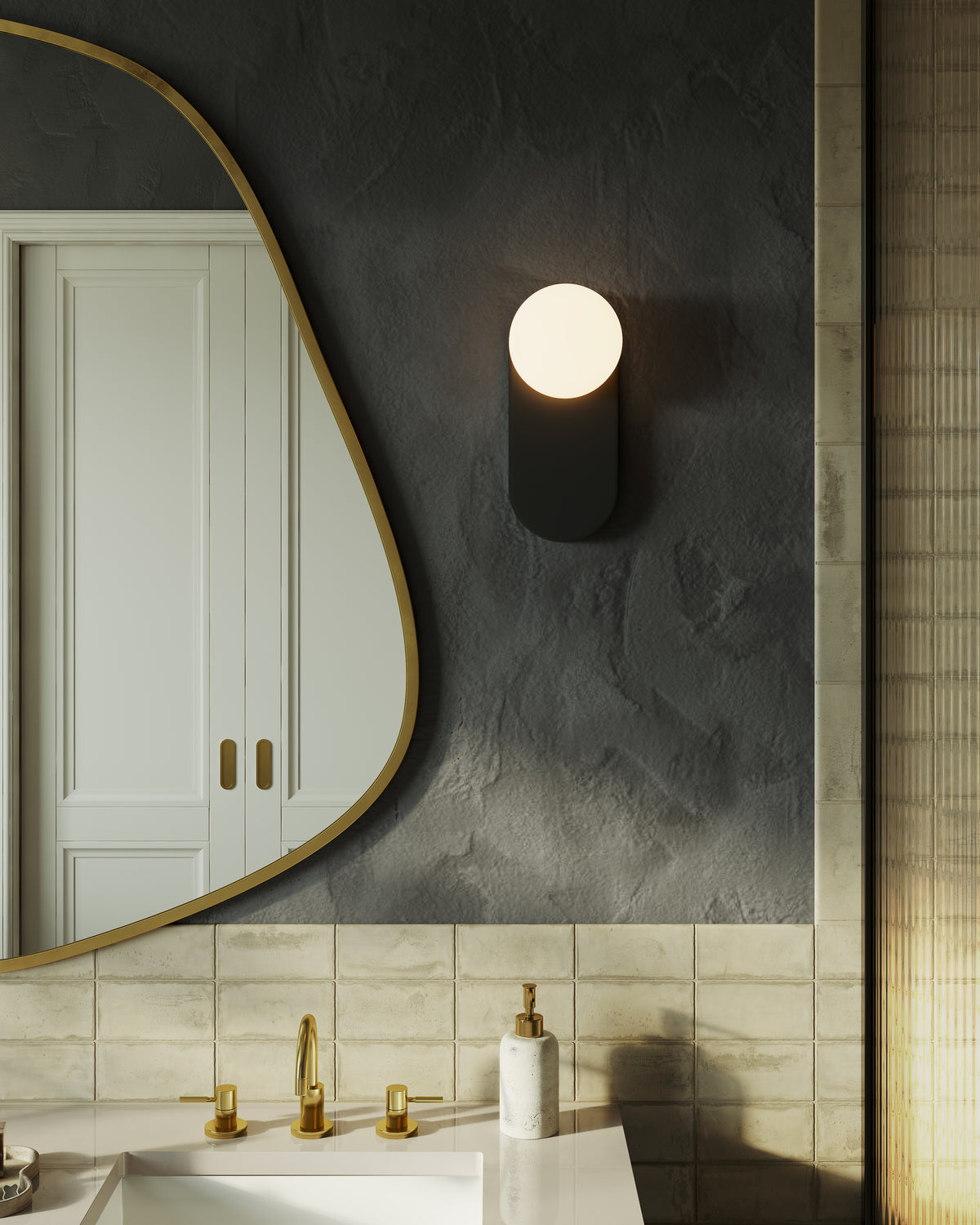 Matte black wall light with rounded backplate and glowing opal globe, mounted beside a sculptural mirror above a tiled vanity