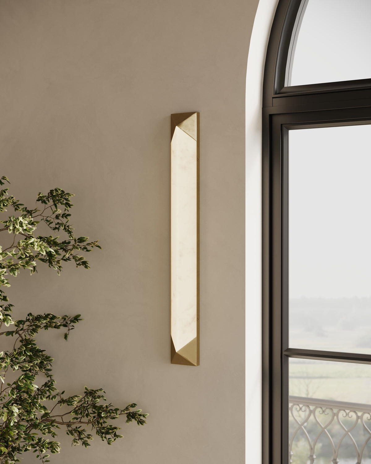 Vertical LED wall sconce with alabaster-style diffuser and brushed brass geometric caps, mounted beside an arched window.