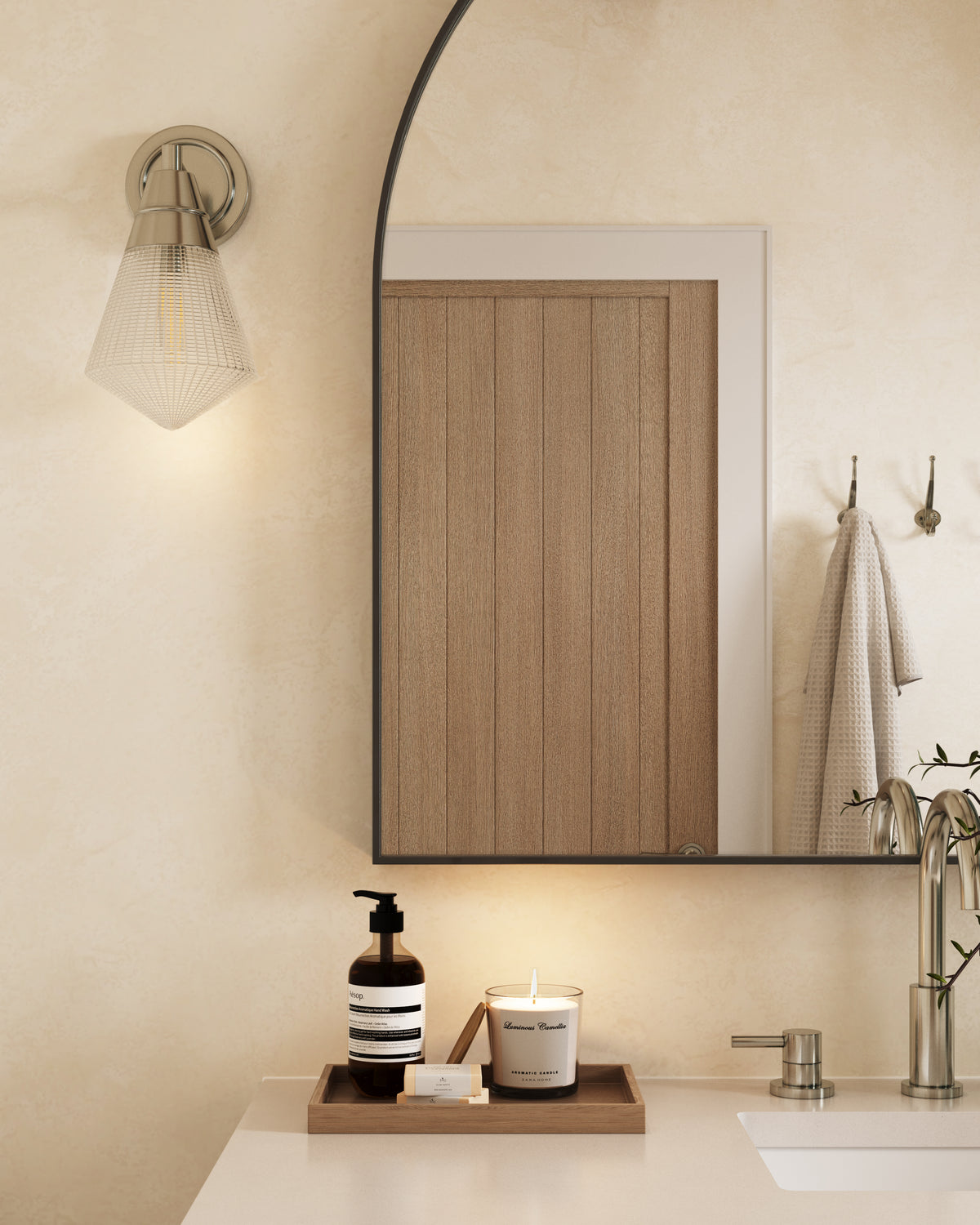Polished chrome wall light with a faceted glass shade softly illuminating a curved mirror above a minimalist bathroom vanity.