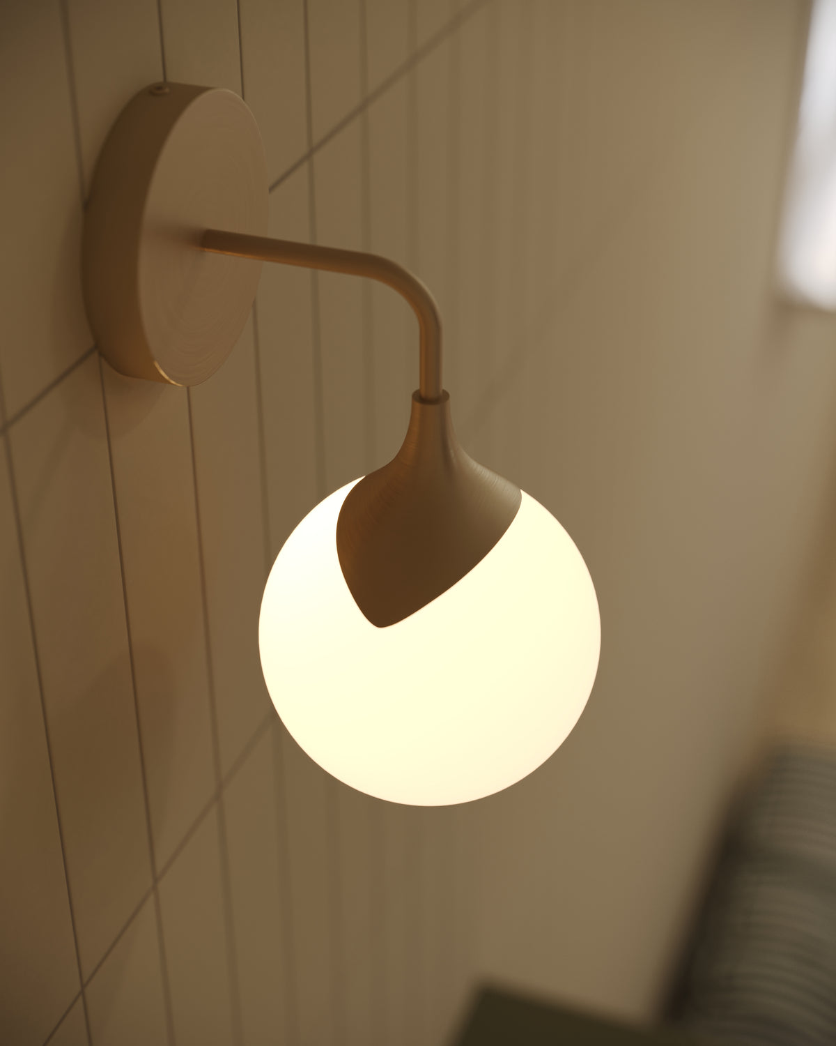 Modern brushed gold wall light with a circular backplate and frosted glass globe shade, creating a sculptural profile with warm ambient illumination.