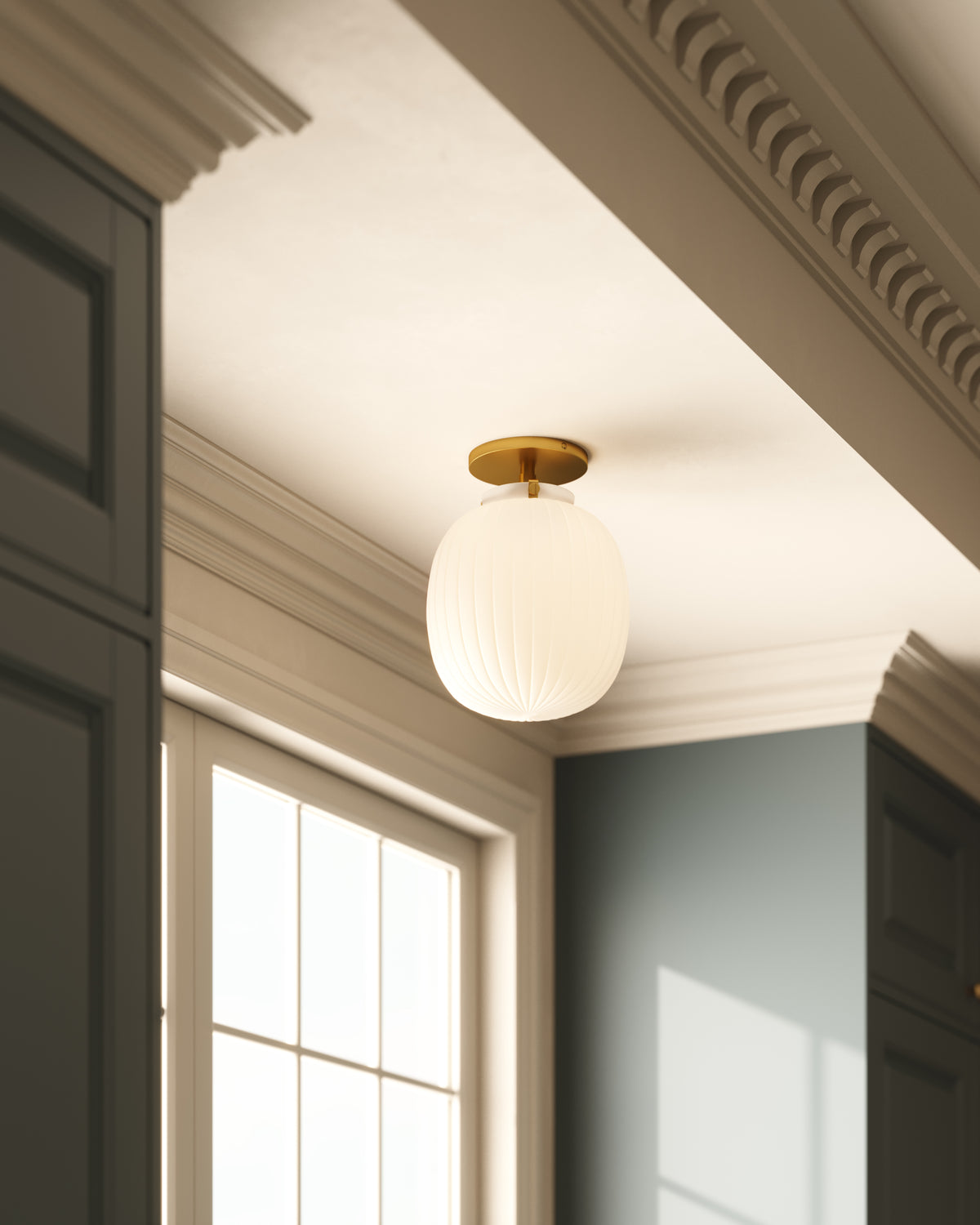 Brushed gold flush mount ceiling light with a glossy ribbed opal glass globe, installed on a white ceiling with decorative crown molding above a window.