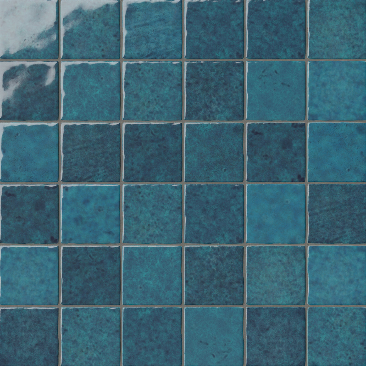 Blue 4x4 ceramic wall tiles installed in a square grid pattern, highlighting organic tonal depth, mottled surface variation, and handcrafted detailing.