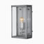 Brushed antique silver wall lantern with a beveled metal frame, clear glass panels, visible glowing bulb, and cool silver interior on a plain white background.
