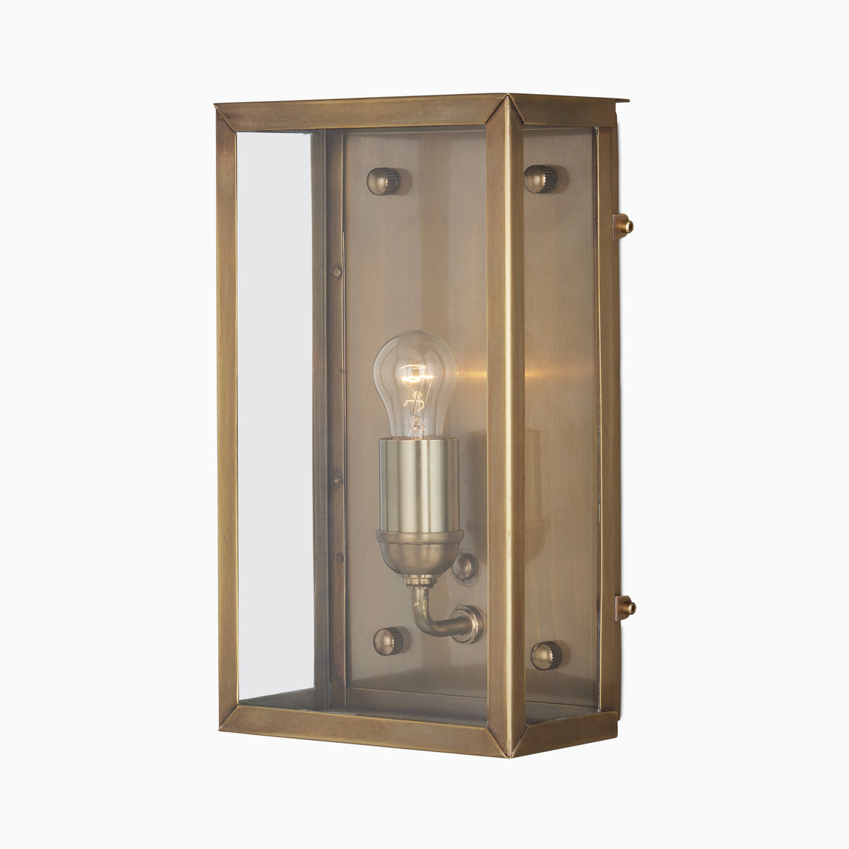 Antique brass wall lantern with a beveled metal frame, clear glass panels, visible glowing bulb, and warm brushed brass interior on a plain white background.