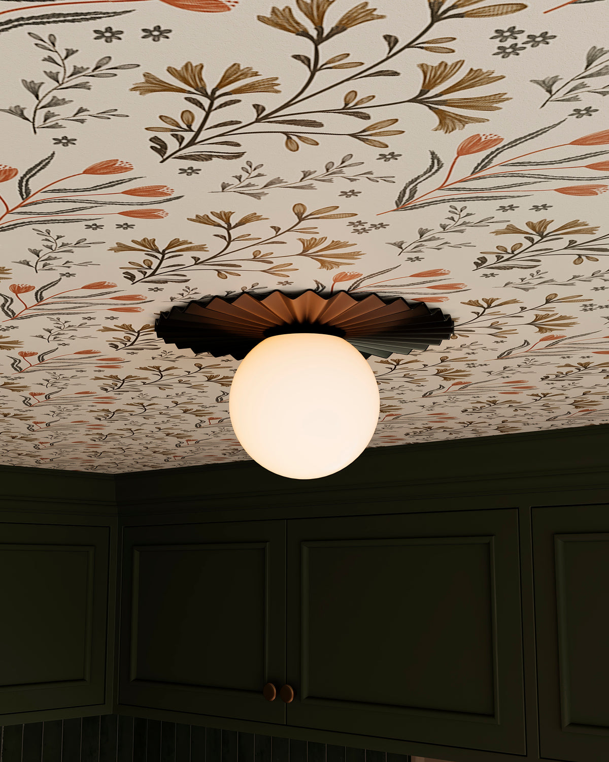 Matte black flush mount ceiling light with a pleated metal shade and glowing globe diffuser installed against botanical wallpaper above dark green cabinetry.
