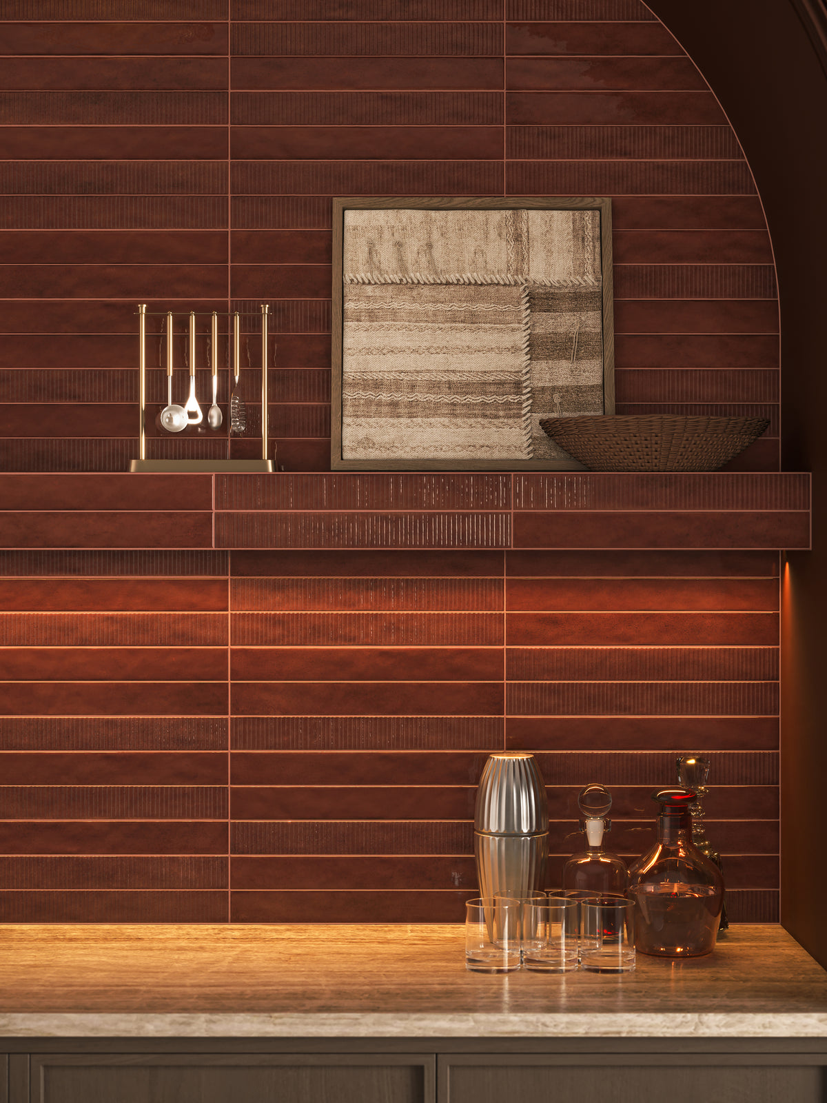 Bar alcove with brown ribbed tile backsplash, floating shelf, framed textile art, brass bar tools, glassware, and warm under-shelf lighting.