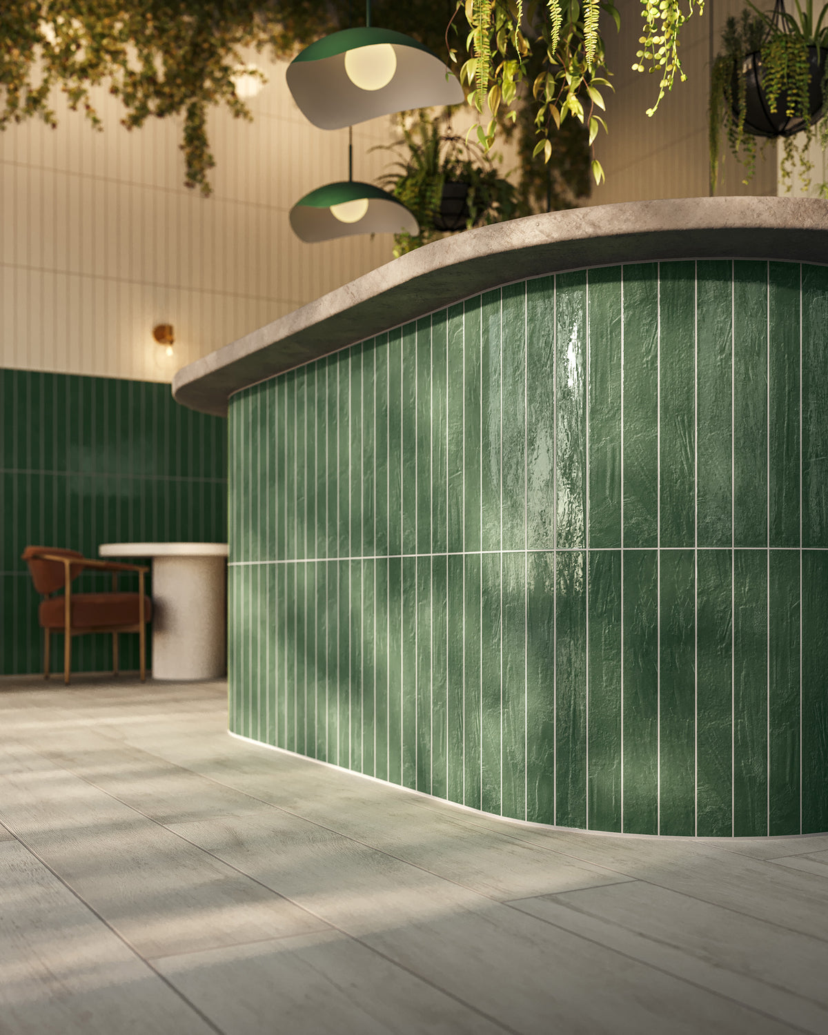 Curved bar front covered in glossy deep green vertical tile with pale grout, topped with a light stone counter and surrounded by cream wall tile, hanging plants, soft green pendant lights, and pale wood-look floor tile.