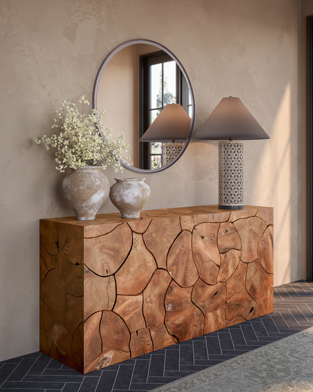 Patterned cream and black table lamp with a dark tapered shade styled on a live-edge wood console beneath a round metal-framed mirror, beside white ceramic vases and pale florals.