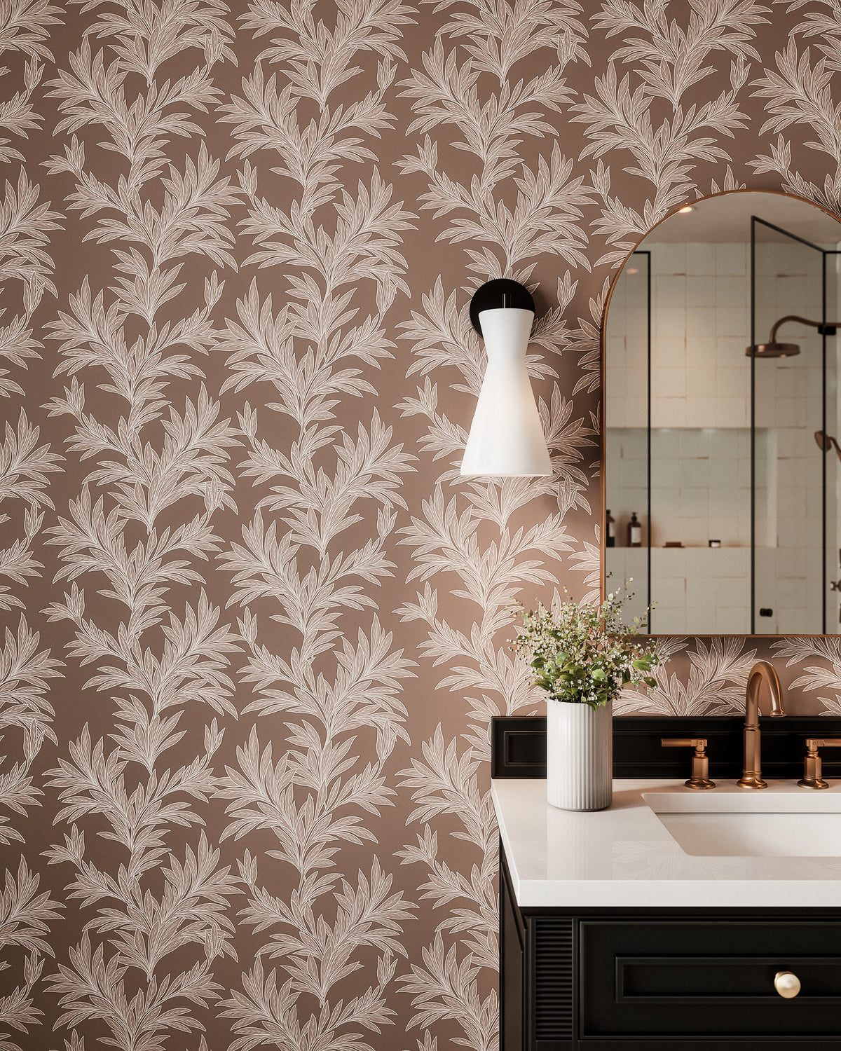 Dark taupe botanical wallpaper with off-white leafy branch pattern, styled in a modern bathroom with an arched mirror, vanity, and wall sconce.