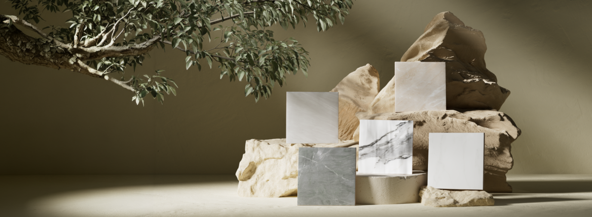 Styled display of five square tile samples in white and gray marble-look finishes arranged on natural stone blocks beneath a leafy tree branch, with warm lighting and soft shadows creating an earthy, modern aesthetic